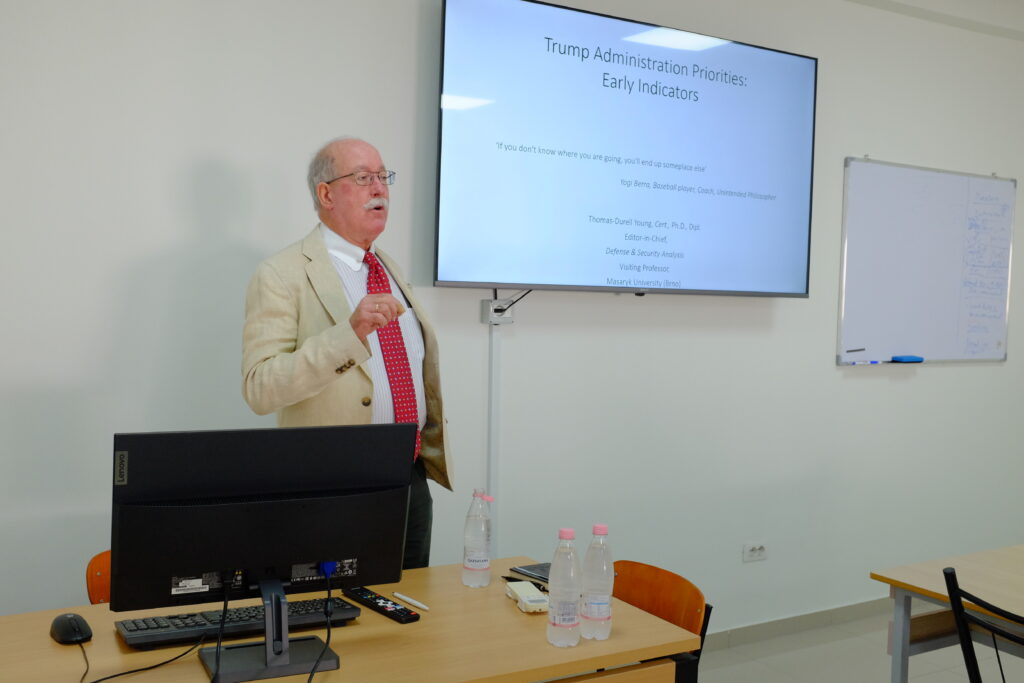 Thomas Durell Young giving a lecture on American Academy of Technology Tirana university. Behind him a screen showing a presentation titled "Trump Administration Priorities: Early Indicators". 
